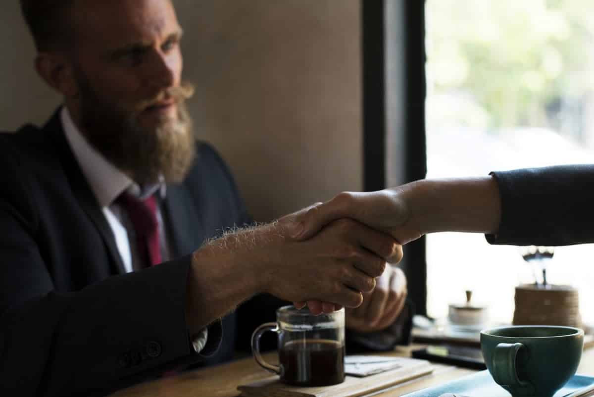 An image of a meeting in which a businessman in a suit is shaking a woman’s hand.