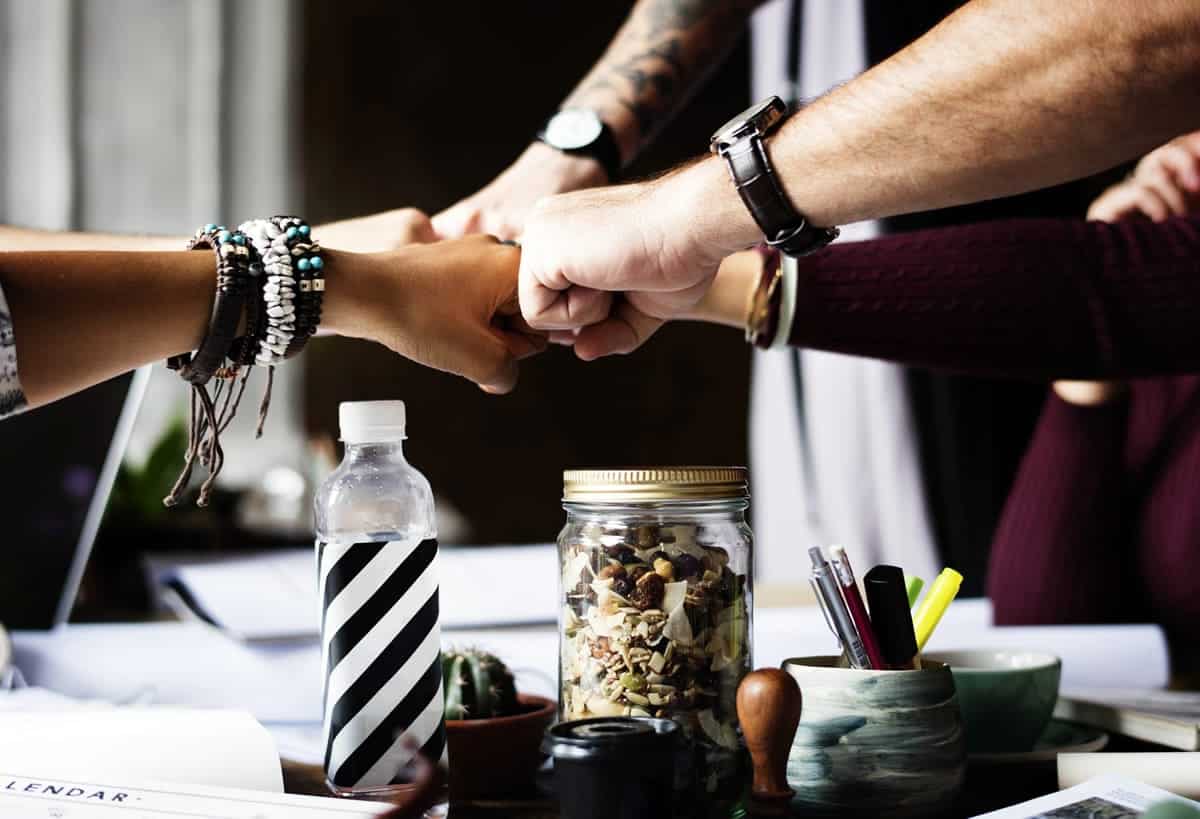 An image of a team fist-bumping in the middle of the table after a meeting.