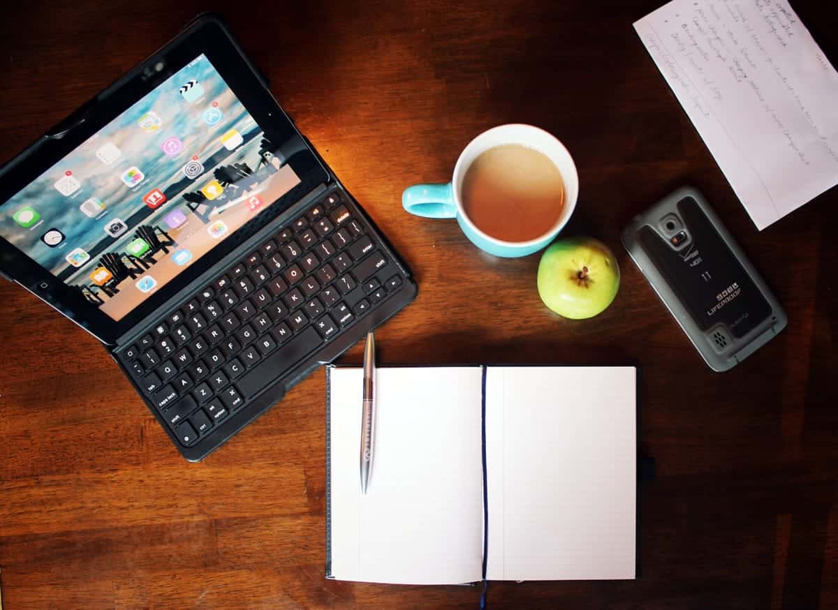 A top-down photo of someone’s workspace, including a tablet, coffee, smartphone, and a notebook.