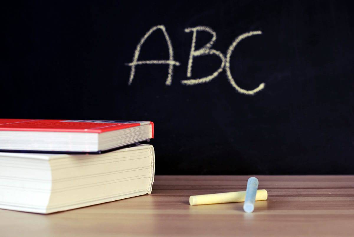 An image chalk and books on a table in front of a chalkboard that shows the letters “ABC”.