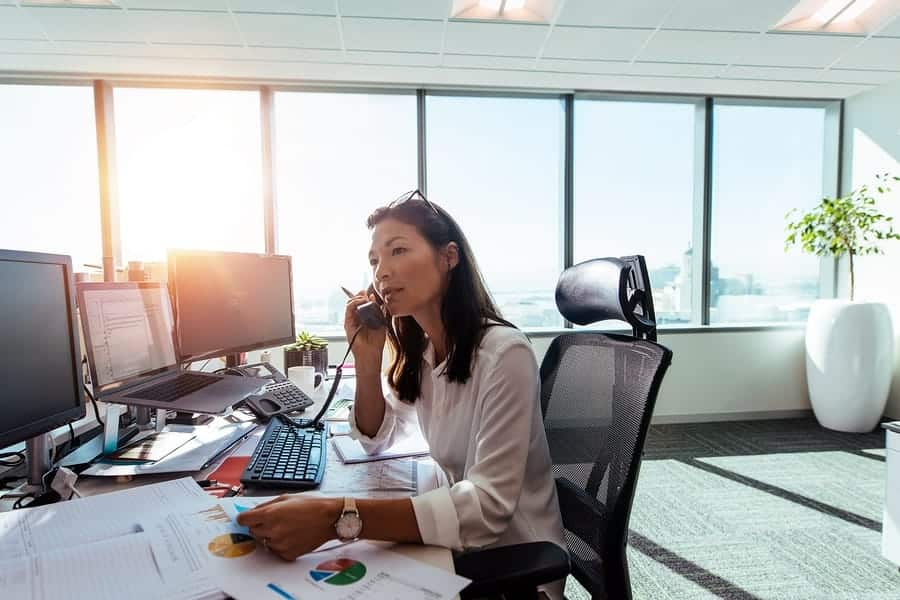 A photo of a woman taking on the phone in her brightly lit office.