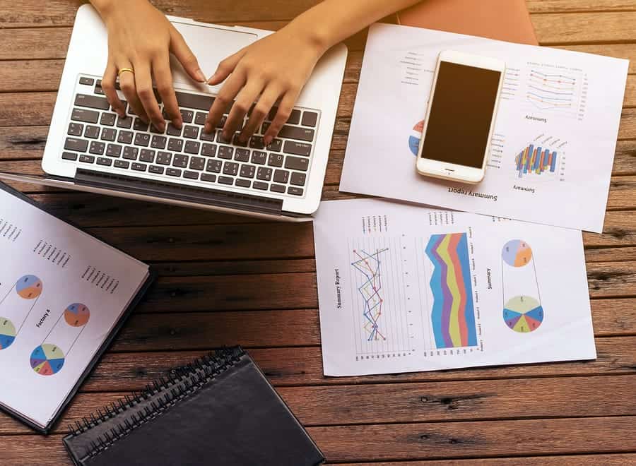 A bird’s eye view of a person’s desk with a laptop, charts, and graphs.