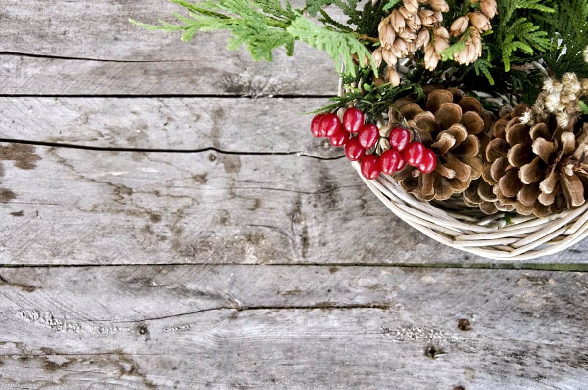 A photo of a centerpiece with dried pinecones and holly in a wicker basket.