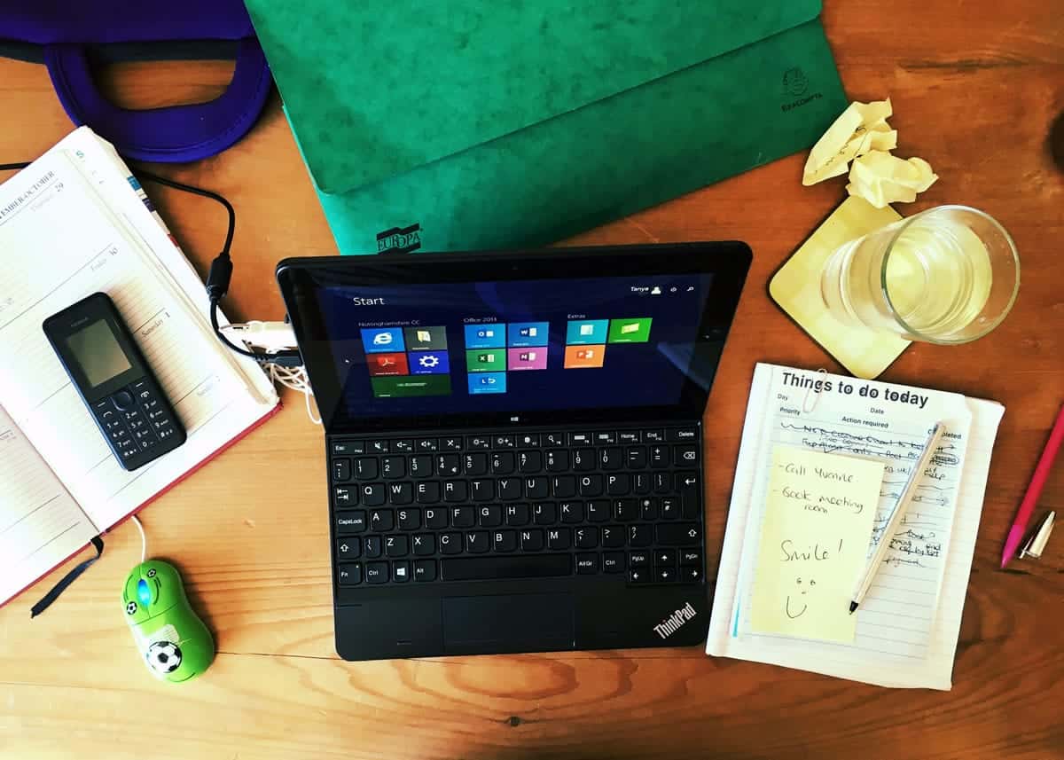 A photo of a person’s desk with a laptop, calendar and to-do list, and water.