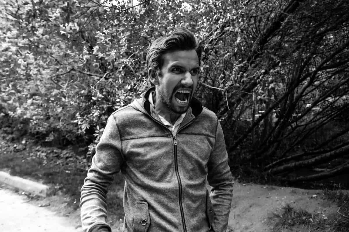 An image of a man outside near trees yelling and frustrated.