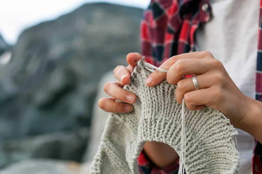 A close-up photo of a woman’s hands knitting on circular needles.