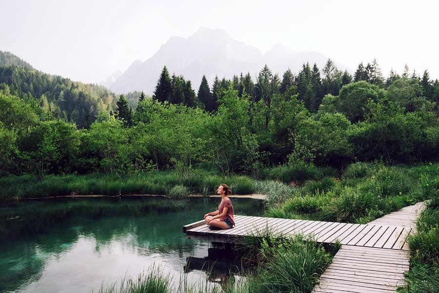 A photo of a person meditating at the end of a short dock on a pond.