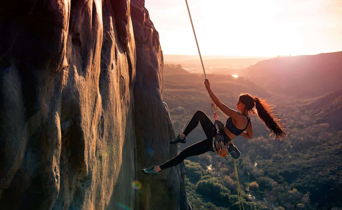 An image of a woman climbing a mountain using a rope.