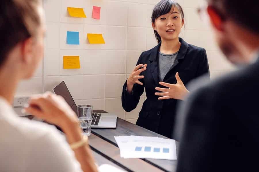 A photo of a woman giving a presentation with sticky notes on the wall behind her.