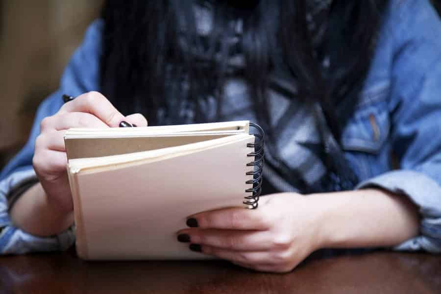 A photo of a woman drawing in a sketch notebook.