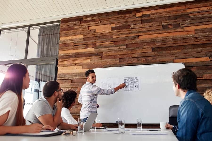 A photo of a man giving a presentation to his design team using a whiteboard.