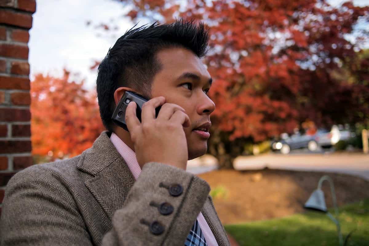 A photo of a man taking a business call on his cell phone outside on an autumn day.