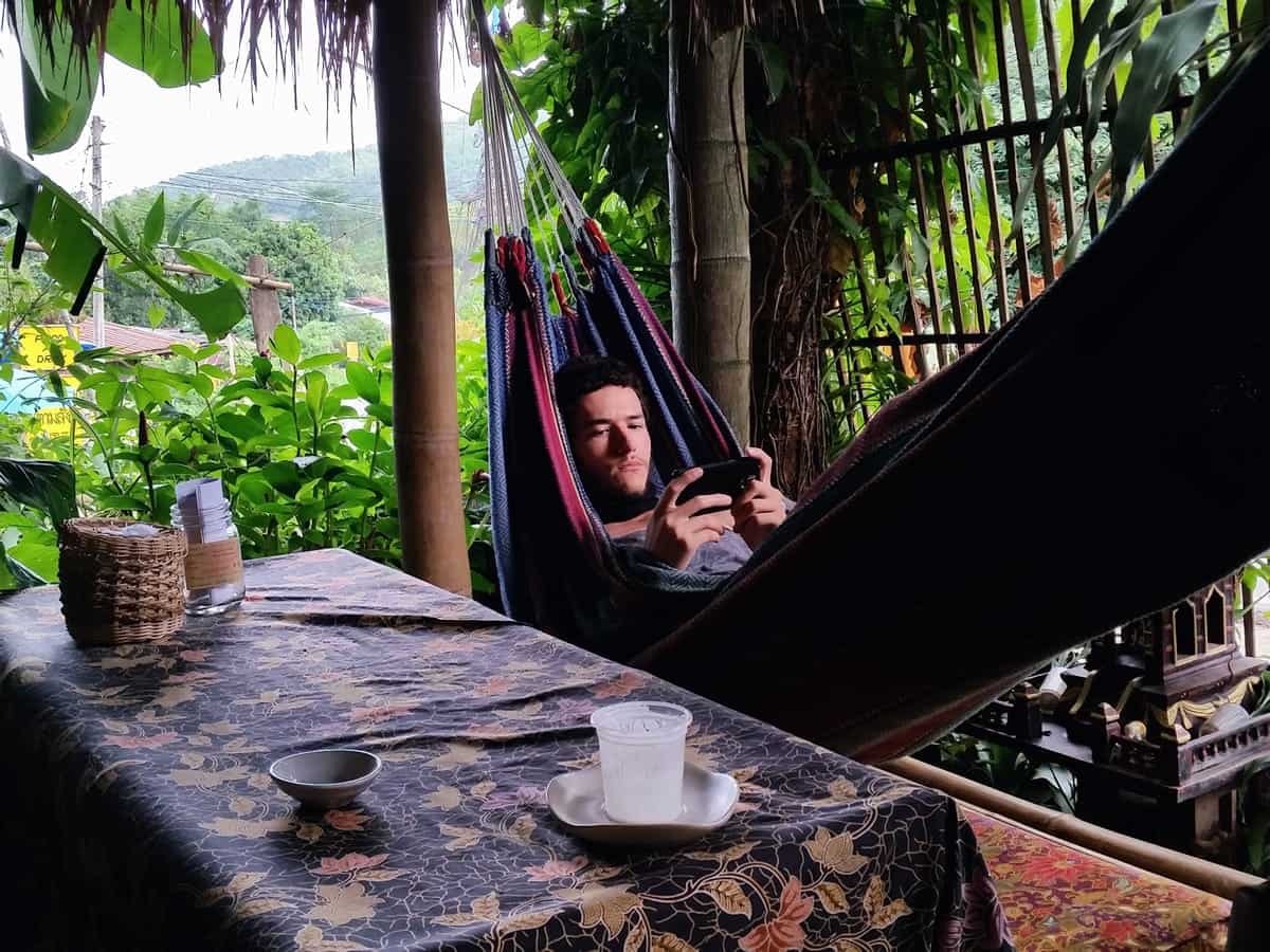 A photo of a man looking at a smartphone while lying in a hammock.
