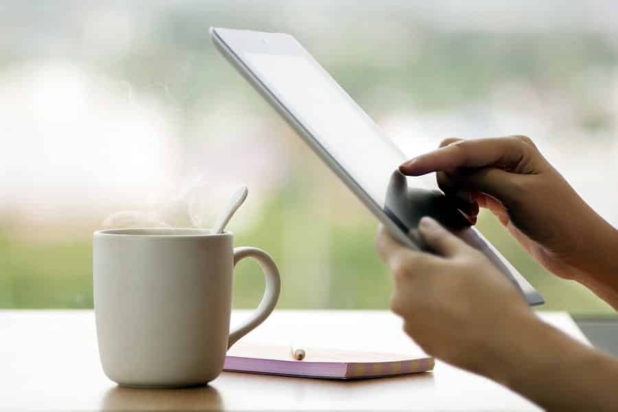 A photo of someone using a tablet while drinking morning coffee.