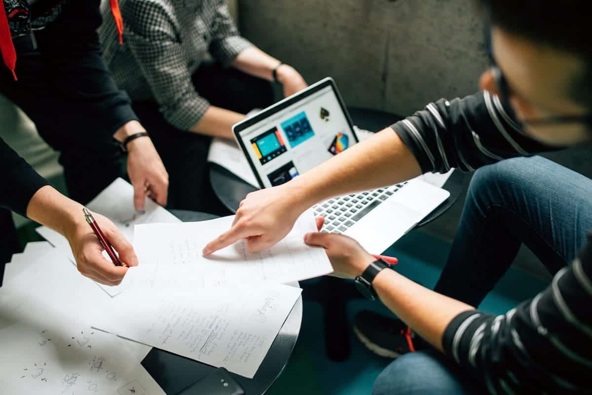 An image of a team meeting together around a computer and paperwork.