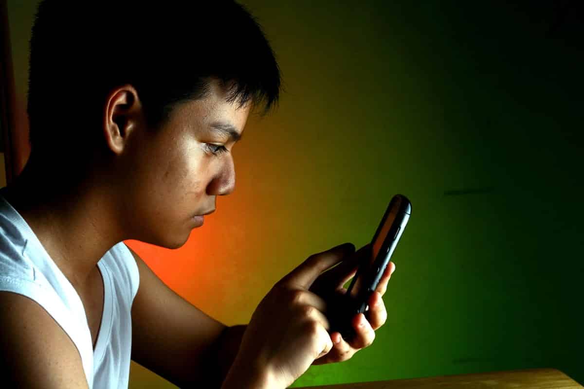 A photo of a teenage boy playing a game on a smartphone.