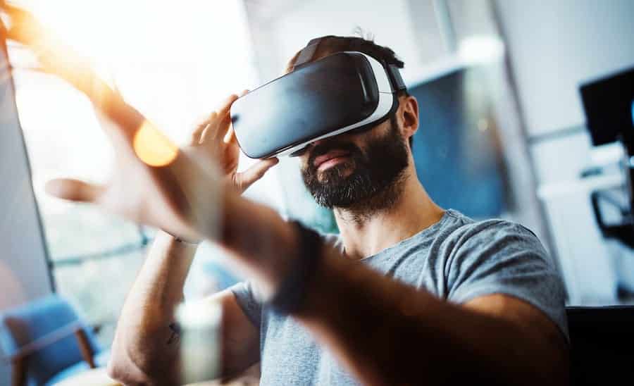 A photo of a man wearing a VR headset, reaching out for something in front of him.