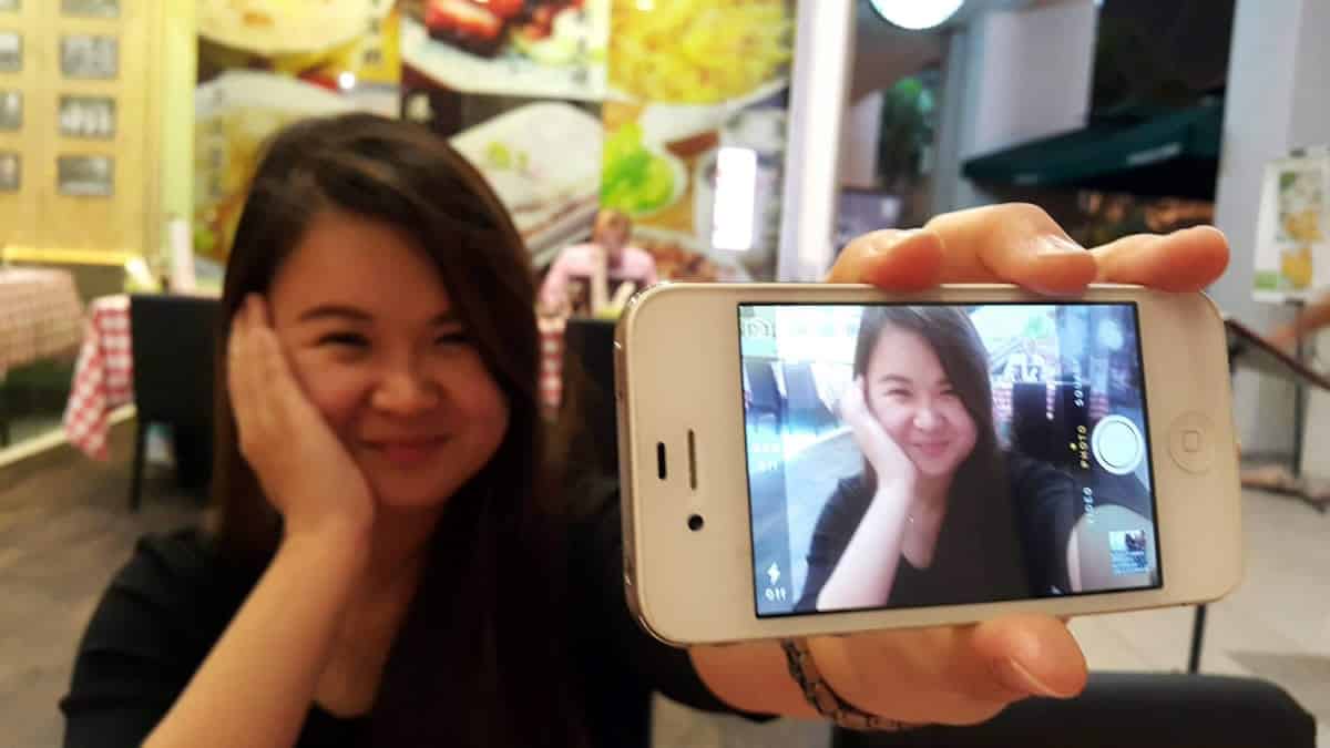 A photo of a woman holding up her smartphone to take a selfie.