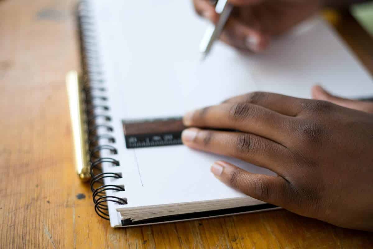 An image of a person drawing a straight line in a notebook with a ruler.