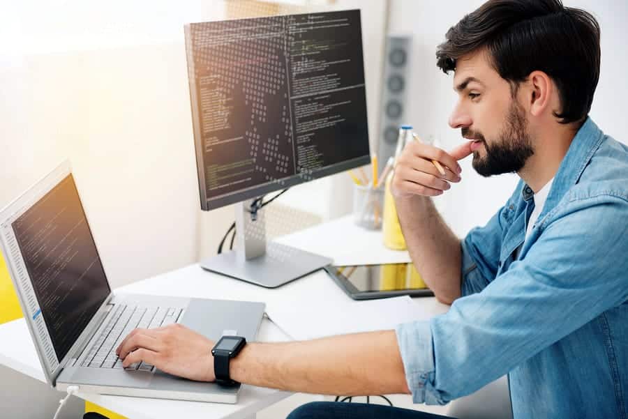 A photo of a mobile app developer in his office with dual computer screens.