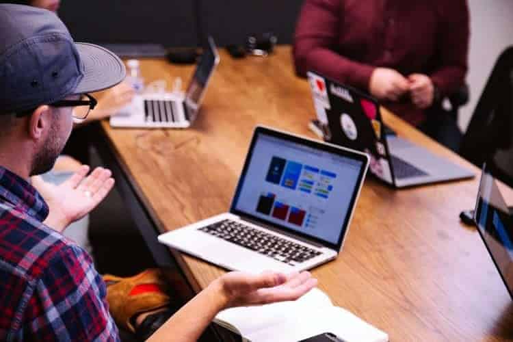 An image of a team meeting around a wooden table with their laptops open.