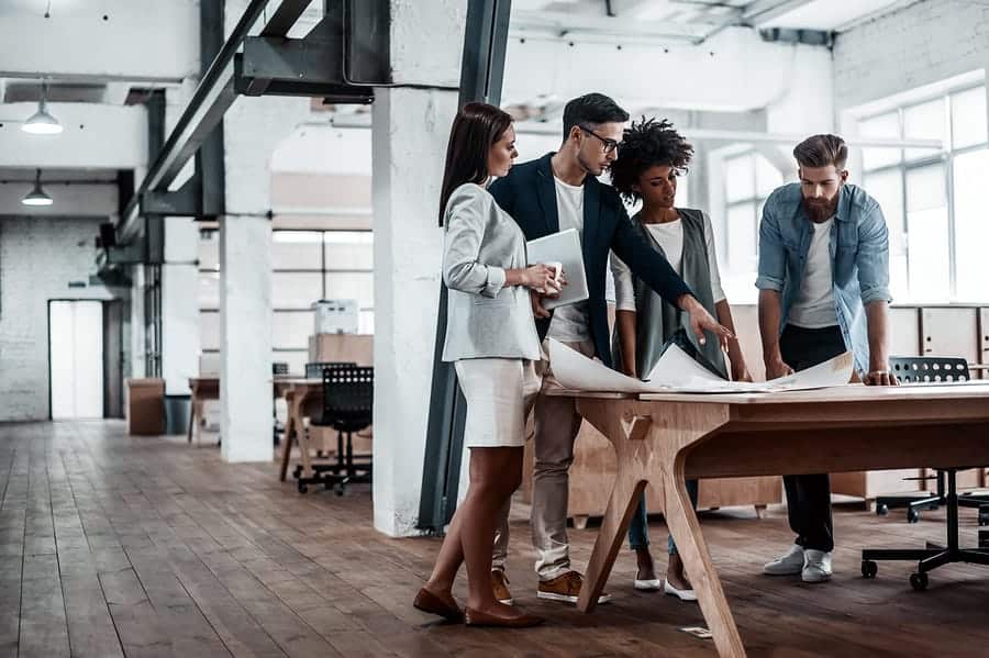 A photo of a design team standing around a large table, looking at drawings.