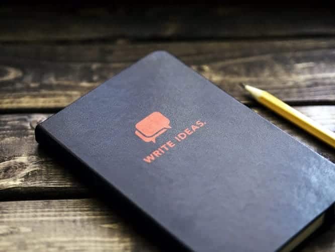 An image of a notebook that says “write ideas” on a wooden table with a pencil.