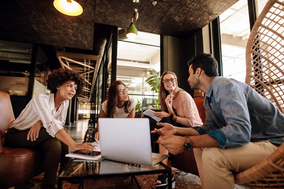 A photo of four young professionals meeting in a modern lobby.