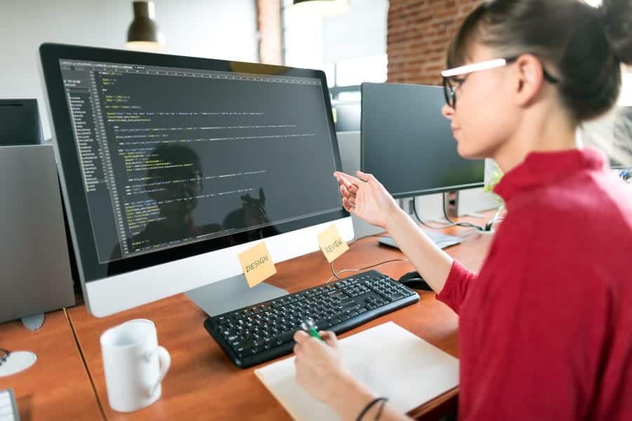 A photo of a young woman working reviewing mobile app code on her computer.