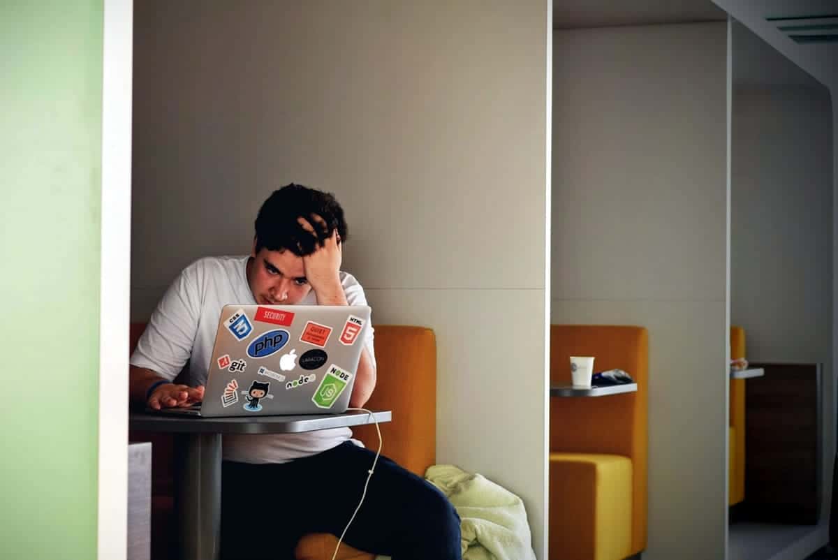 a Frustrated man with hand on head as he sits at a table with his laptop.