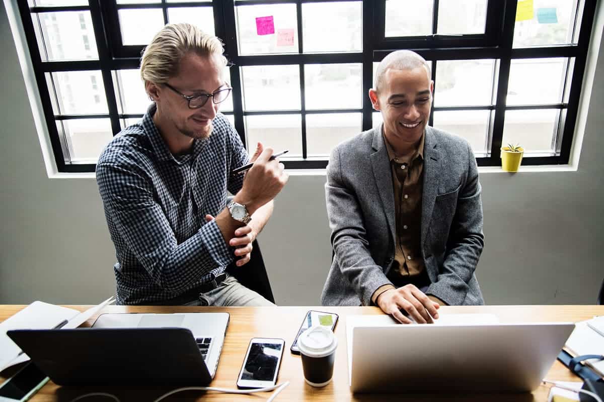 Two men smiling and looking at a laptop during a meeting.