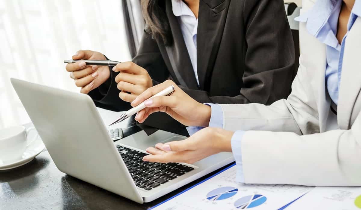 A photo of two women looking at a laptop and having a discussion.