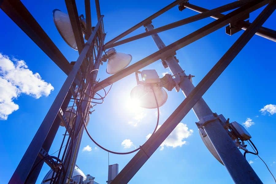 A photo looking up into a communications tower with a sunny sky in the background.