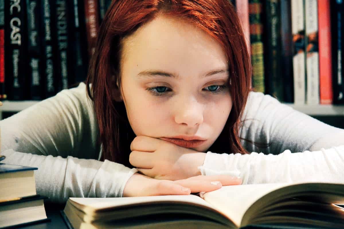 A photo of a teenager resting her chin on her hands while reading a book.