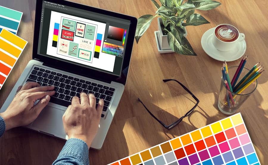 A photo of a graphic designer working at a laptop, surrounded by color swatch samples.