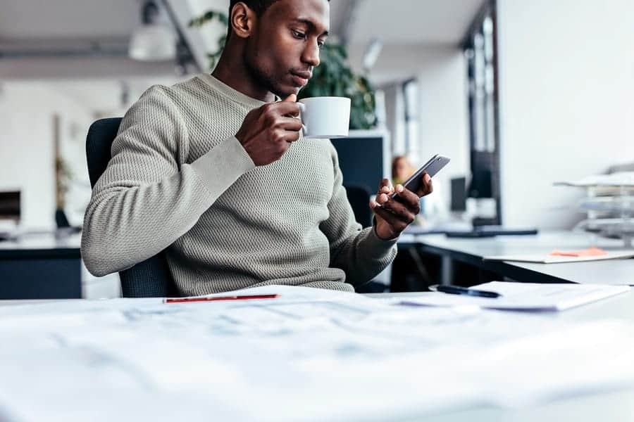 A photo of a man checking notifications on his smartphone while drinking coffee.