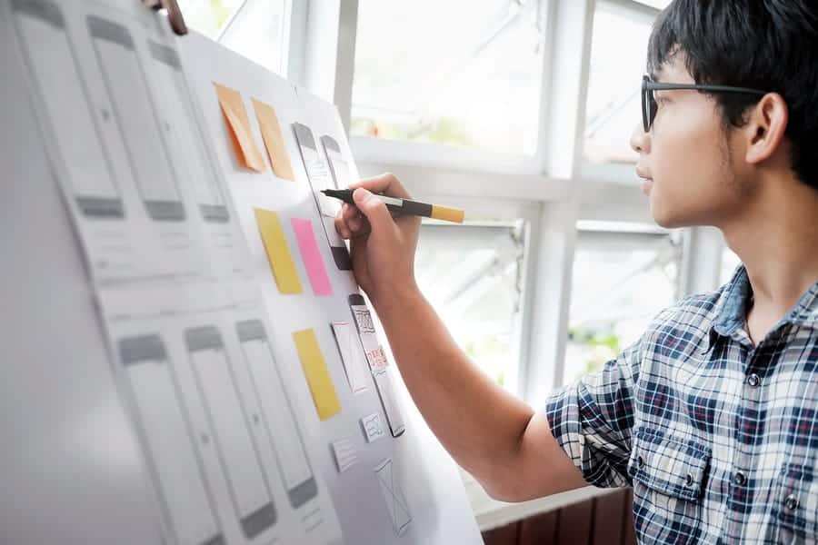 A photo of a man making notes about the latest mobile app design on a piece of posterboard.