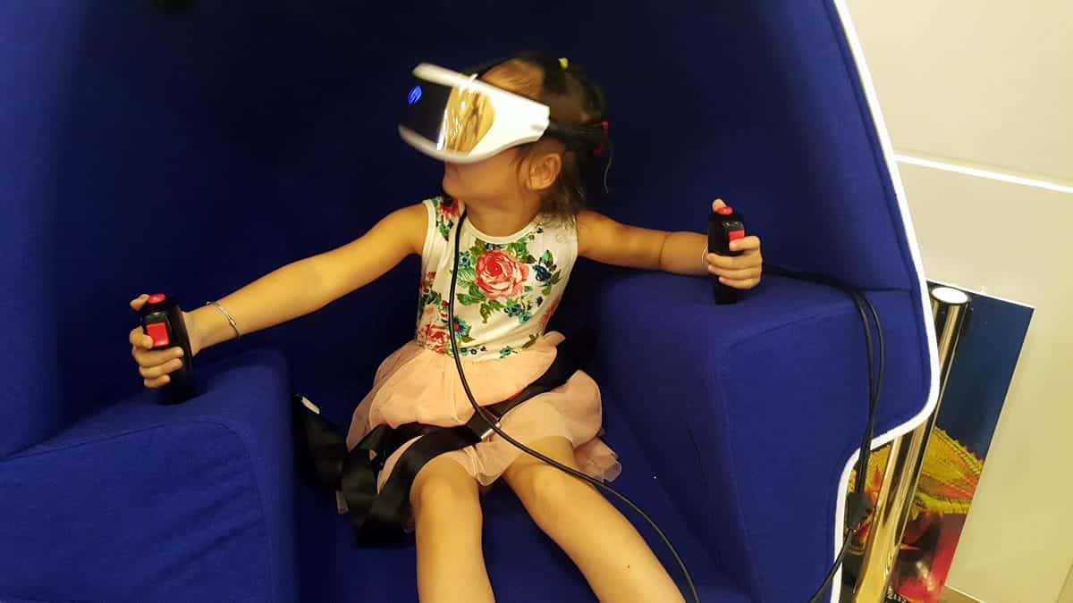 A photo of a young girl trying out a virtual reality headset with hand controls.
