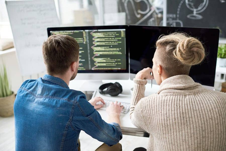 A photo of two developers looking at lines of code on a computer monitor.