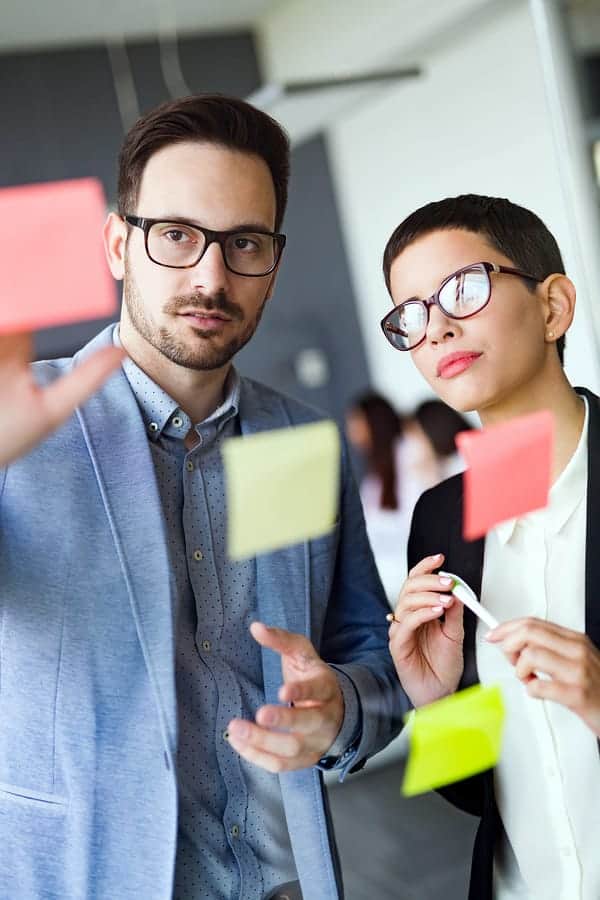 A photo of two team members organizing sticky notes on a pane of glass.