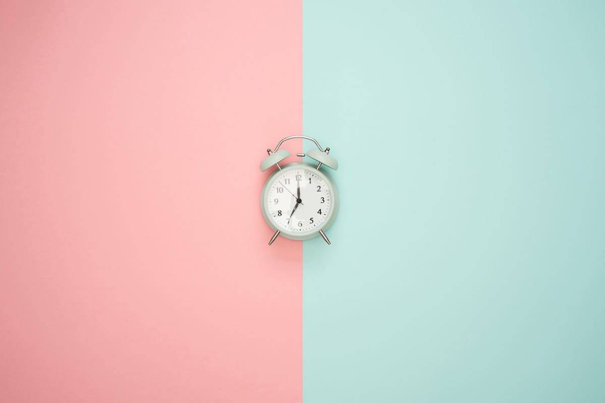 A clock on a pastel pink and mint background.