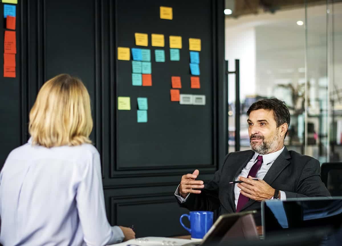 A woman and man meeting with a wall of post its behind them.