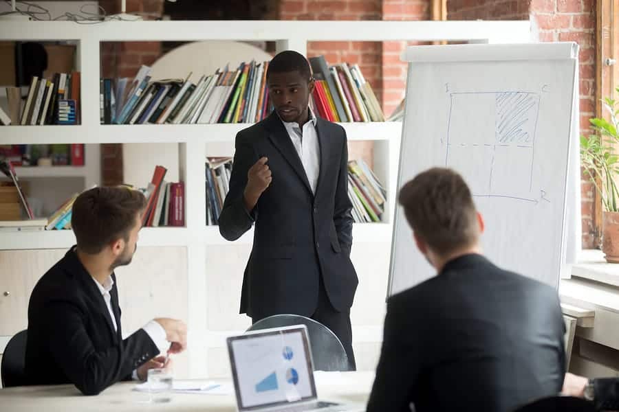 A photo of a man making a presentation to two other men in an office.