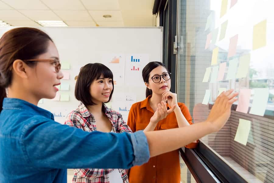 A photo of three mobile app developers rearranging sticky notes on a window.