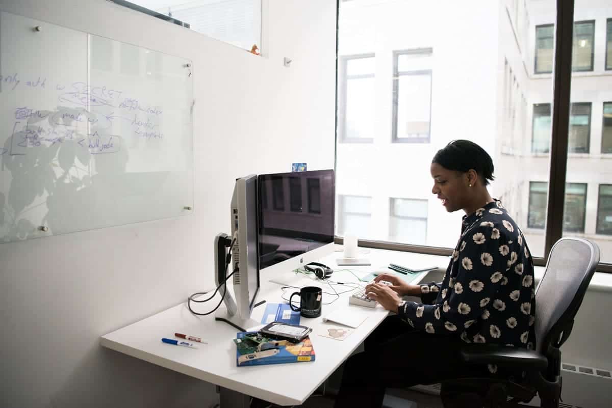 A woman typing at her desk in front of two monitors.