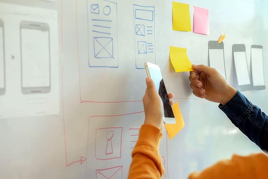 A photo of people moving sticky notes around on a whiteboard.