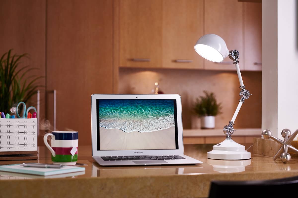 A photo of the OttLite LED Revive Desk Lamp on a desk next to a laptop and a mug of hot tea.