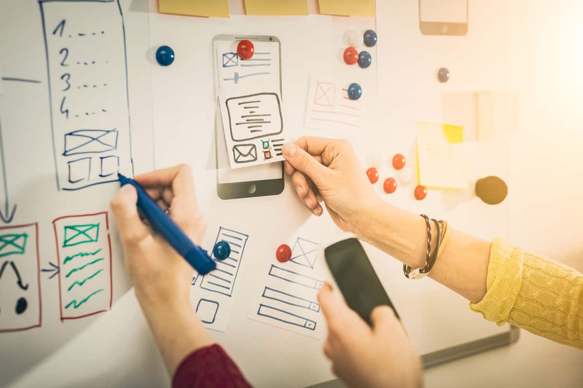 A photo of coworkers using a dry erase board to work on their latest mobile app design.