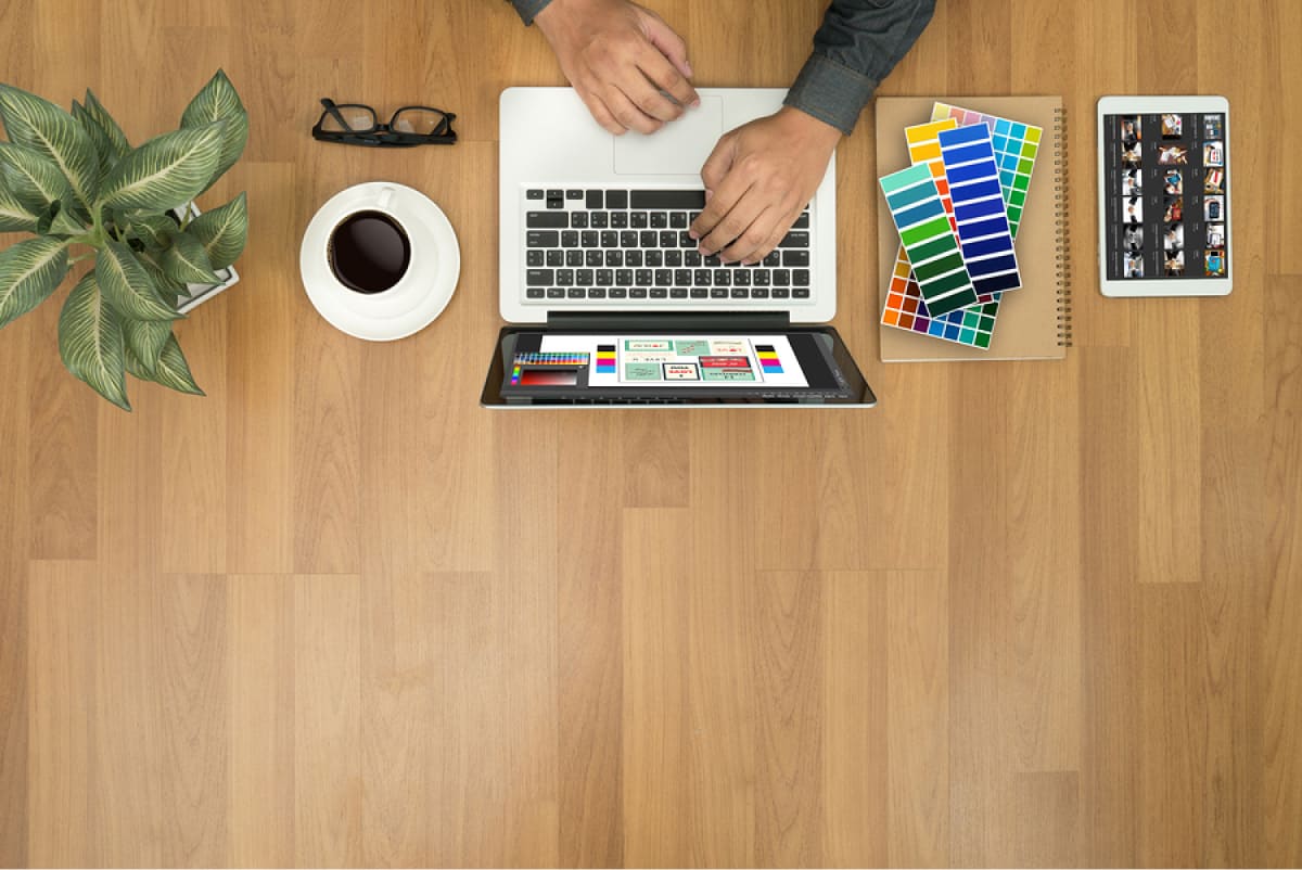 A photo of a mobile app designer sitting at his desk with a laptop, coffee, and color swatches.