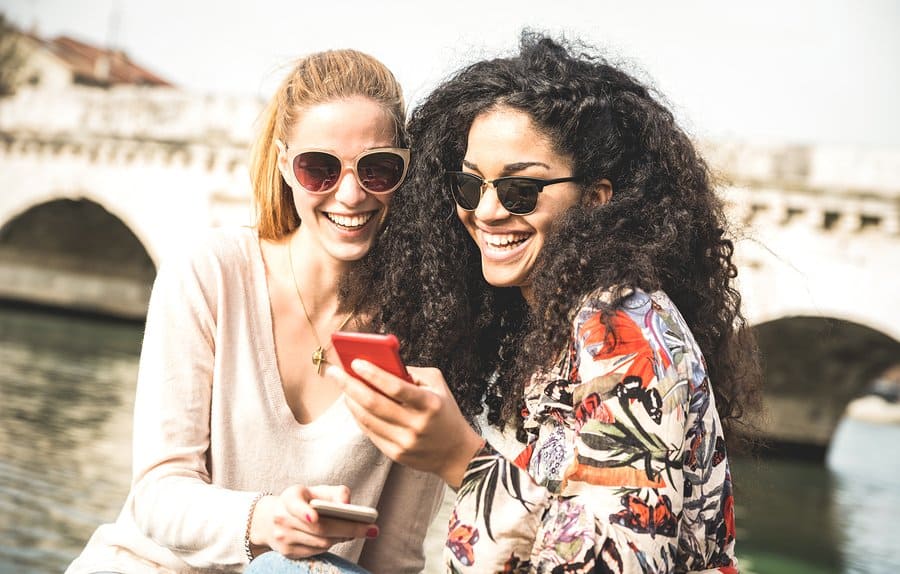 A photo of two women looking at a smartphone and laughing together.